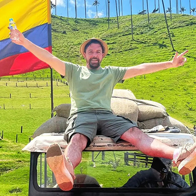 Länderexperte Norman Paraiso sitzt in Kolumbien auf einem Auto und grinst in die Kamera